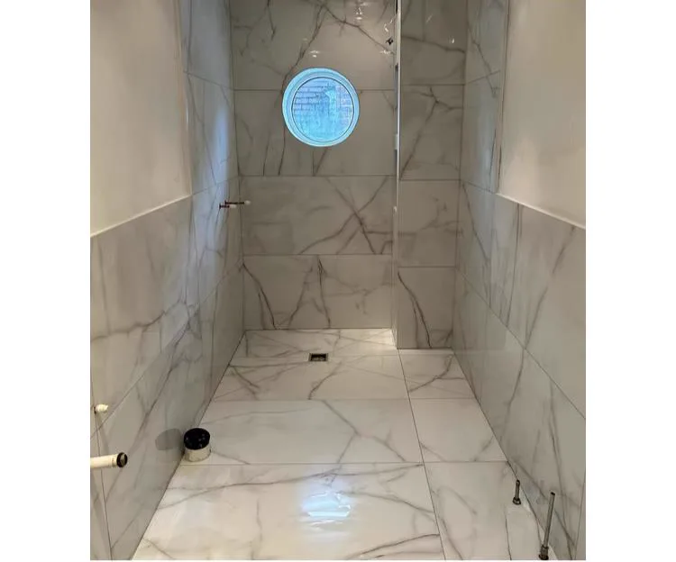 Marble-effect wet room with porthole window, floor-to-ceiling porcelain tiles, Banks and Co Ceramics installation