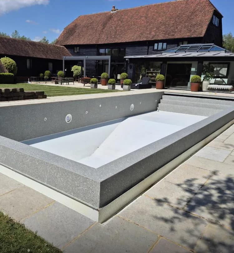 Grey terrazzo-effect coping tiles around an outdoor swimming pool at a Sussex barn conversion property